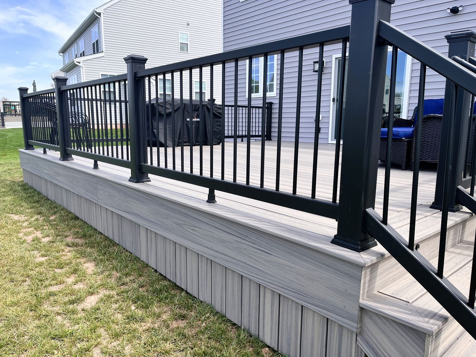 A deck with a black railing and stairs in front of a house.