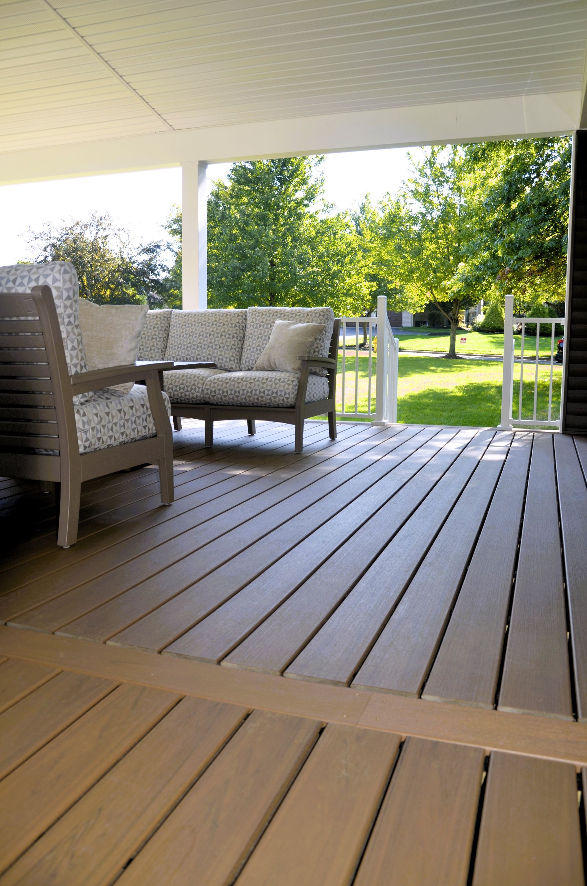 Covered porch with wicker chairs, a wooden deck, and a sunny green yard beyond the railing