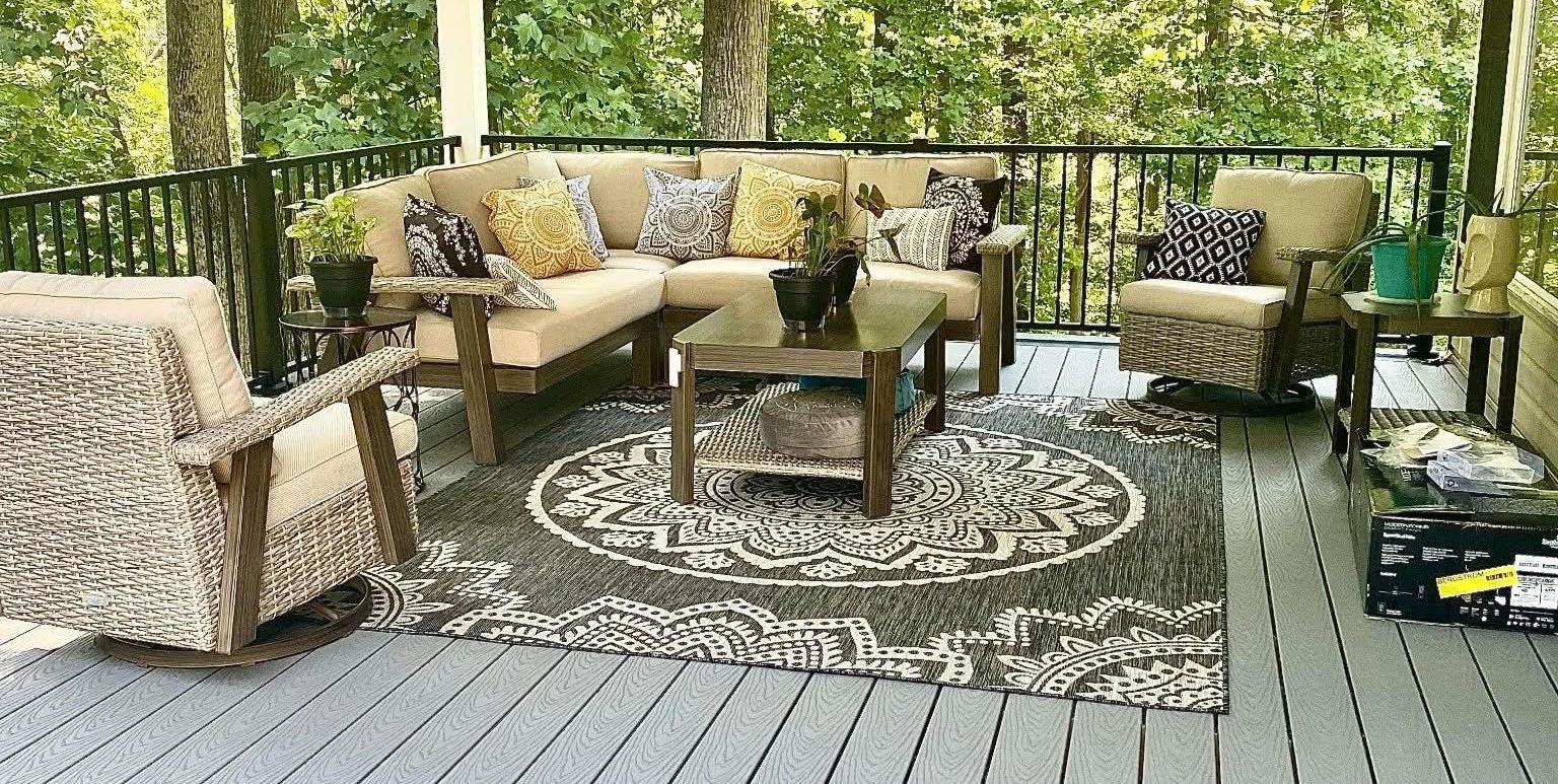 A deck with a couch , chairs , and a rug on it.