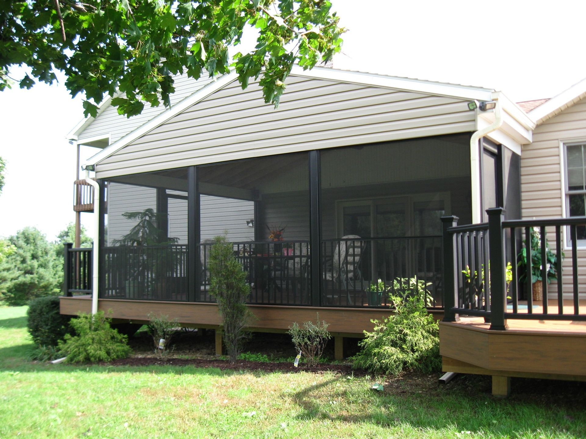 Screened porch attached to a house with black railings and dark screens, on a wooden deck.