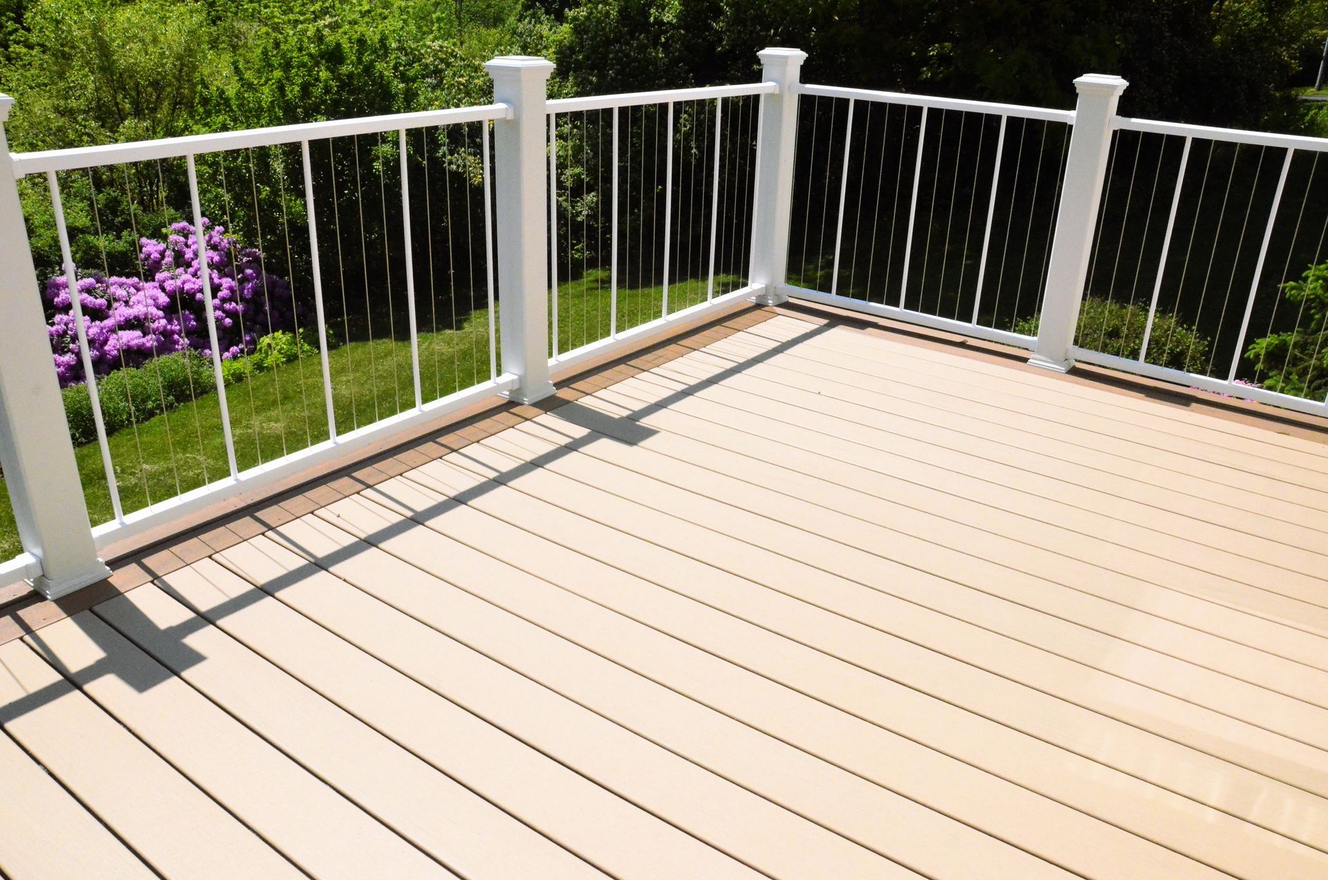 Wooden deck with white railing, surrounded by green foliage.