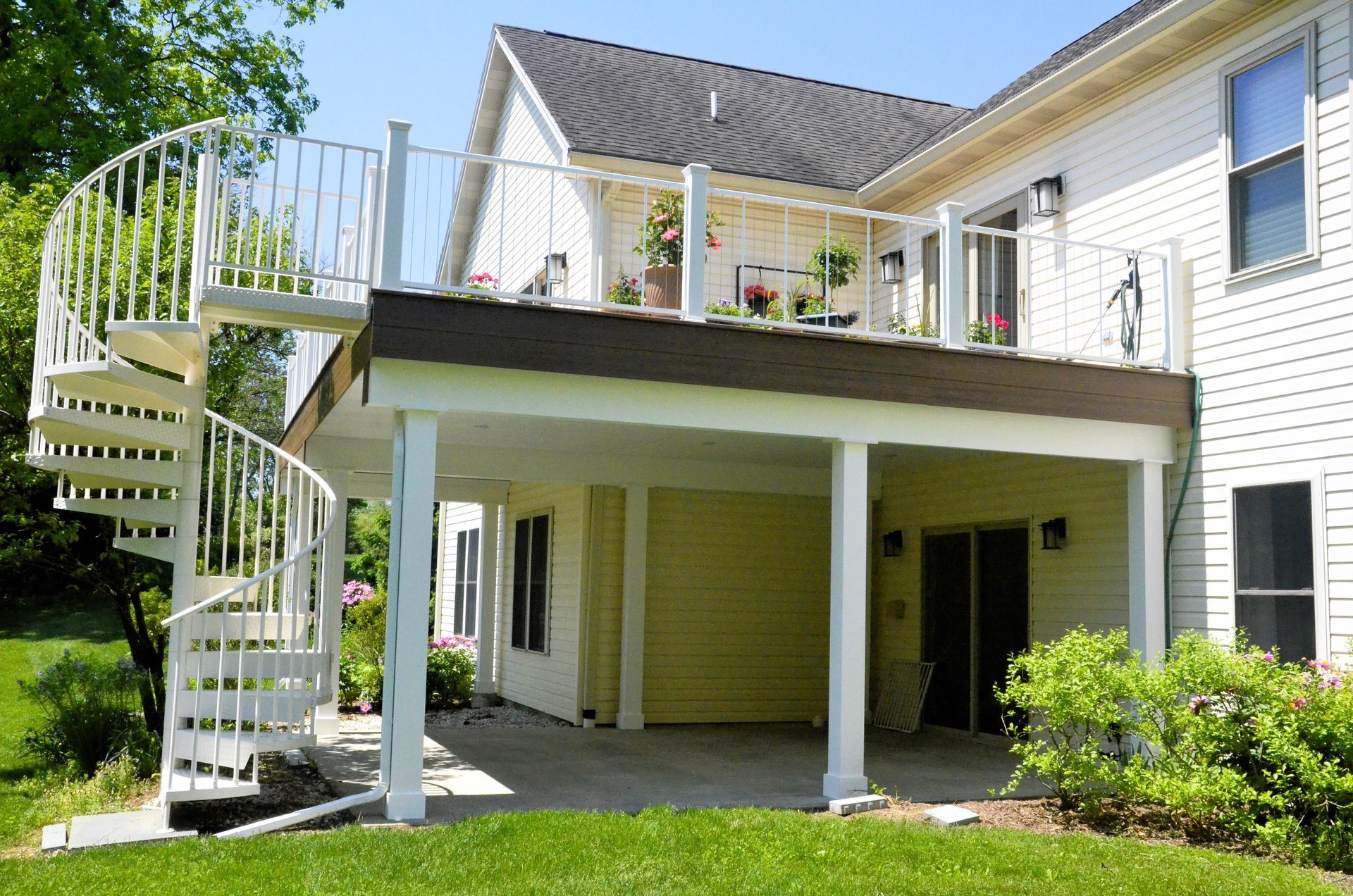 White spiral staircase leads to a deck on the second story of a two-story house with a green lawn.