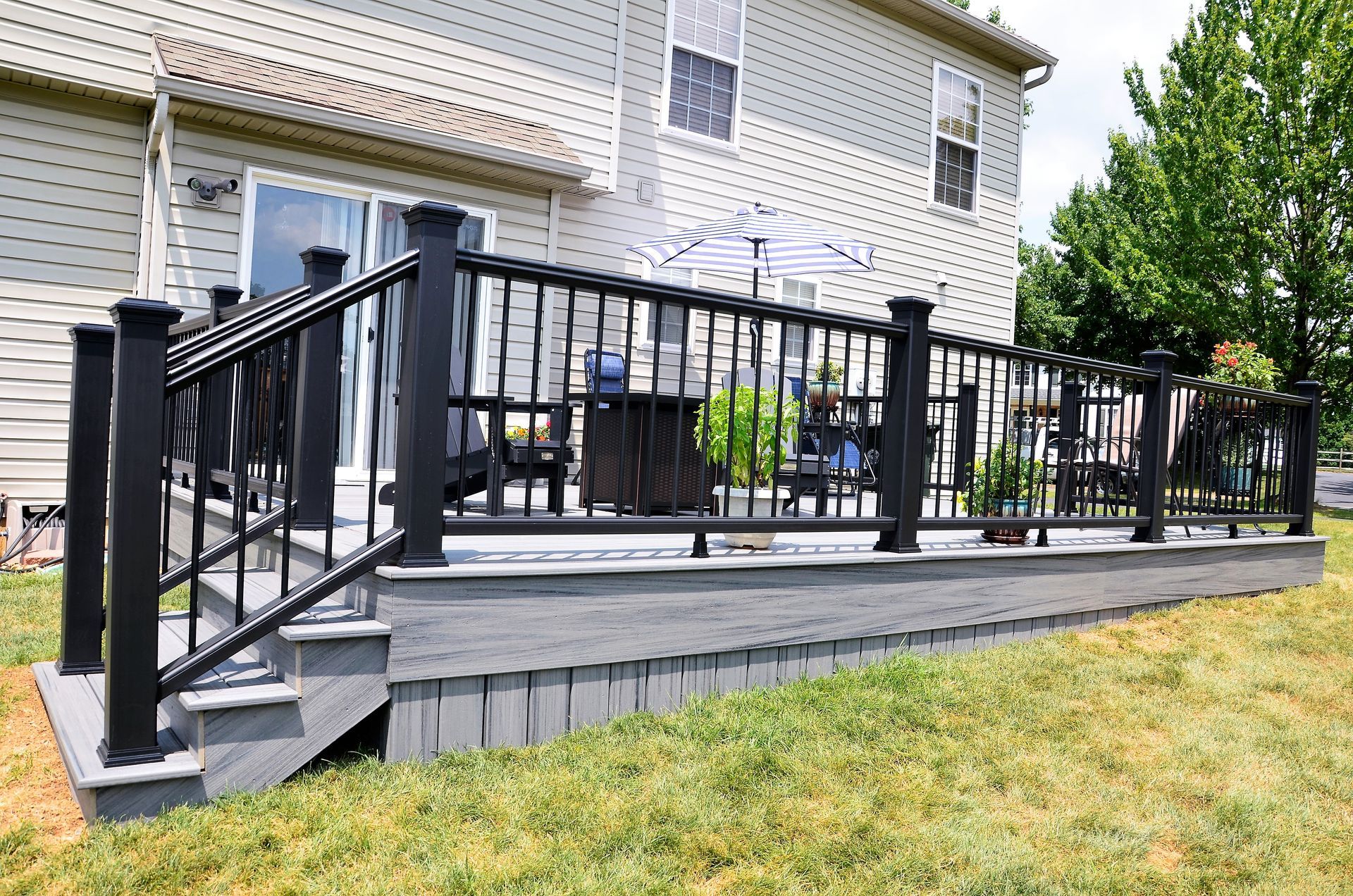 Black deck with railing, stairs, and composite boards against a light-colored house. Green grass in the yard.