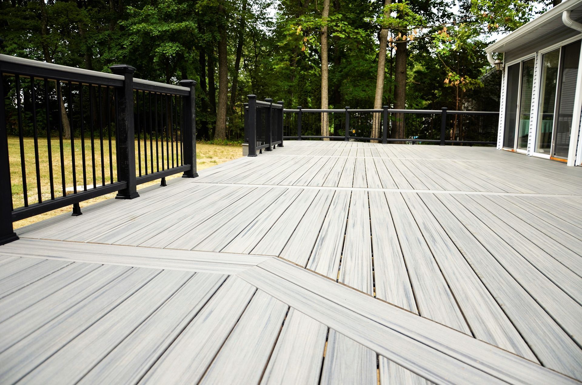 A large wooden deck with a black railing and trees in the background.