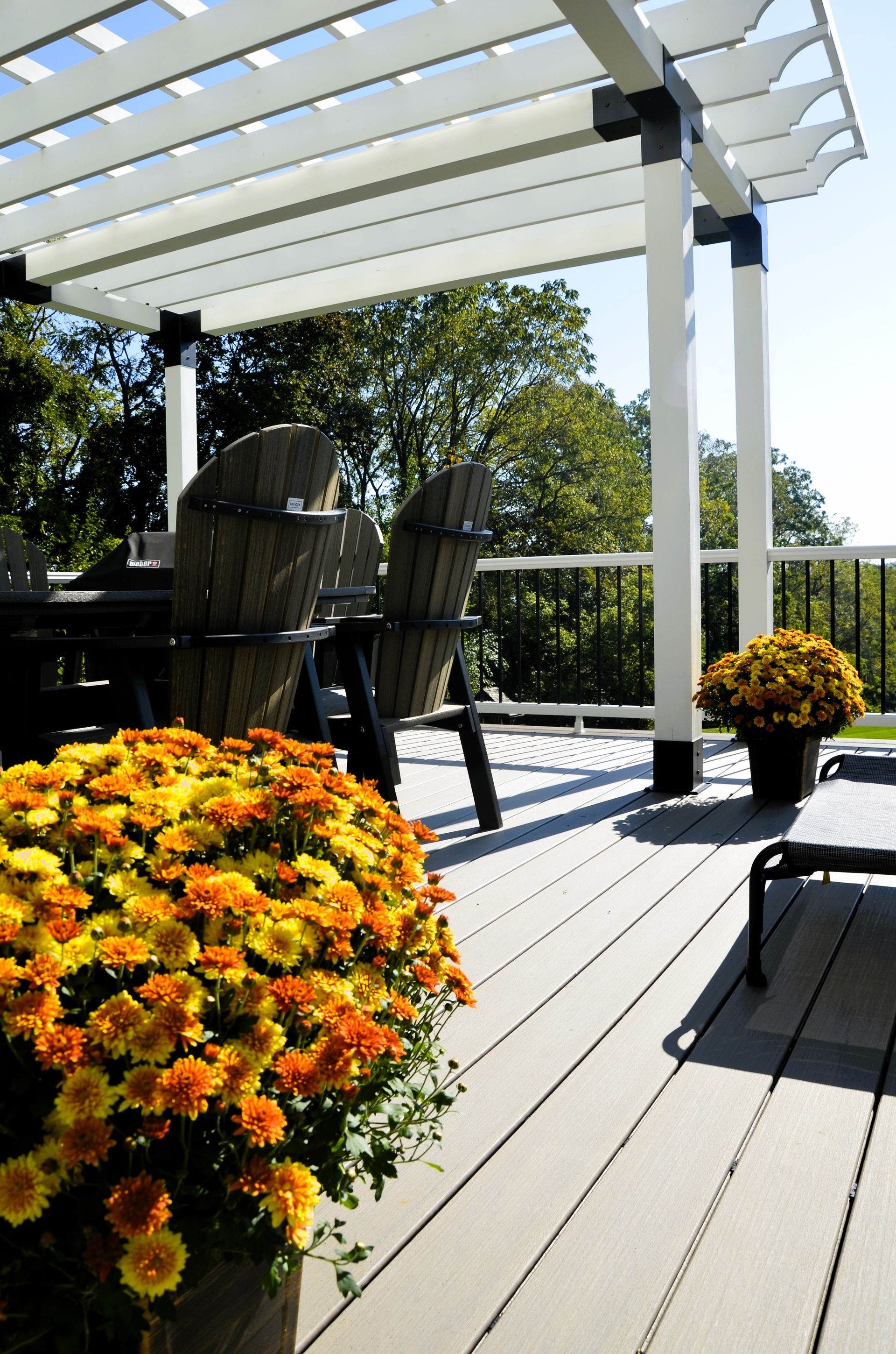 A deck with chairs and flowers under a pergola
