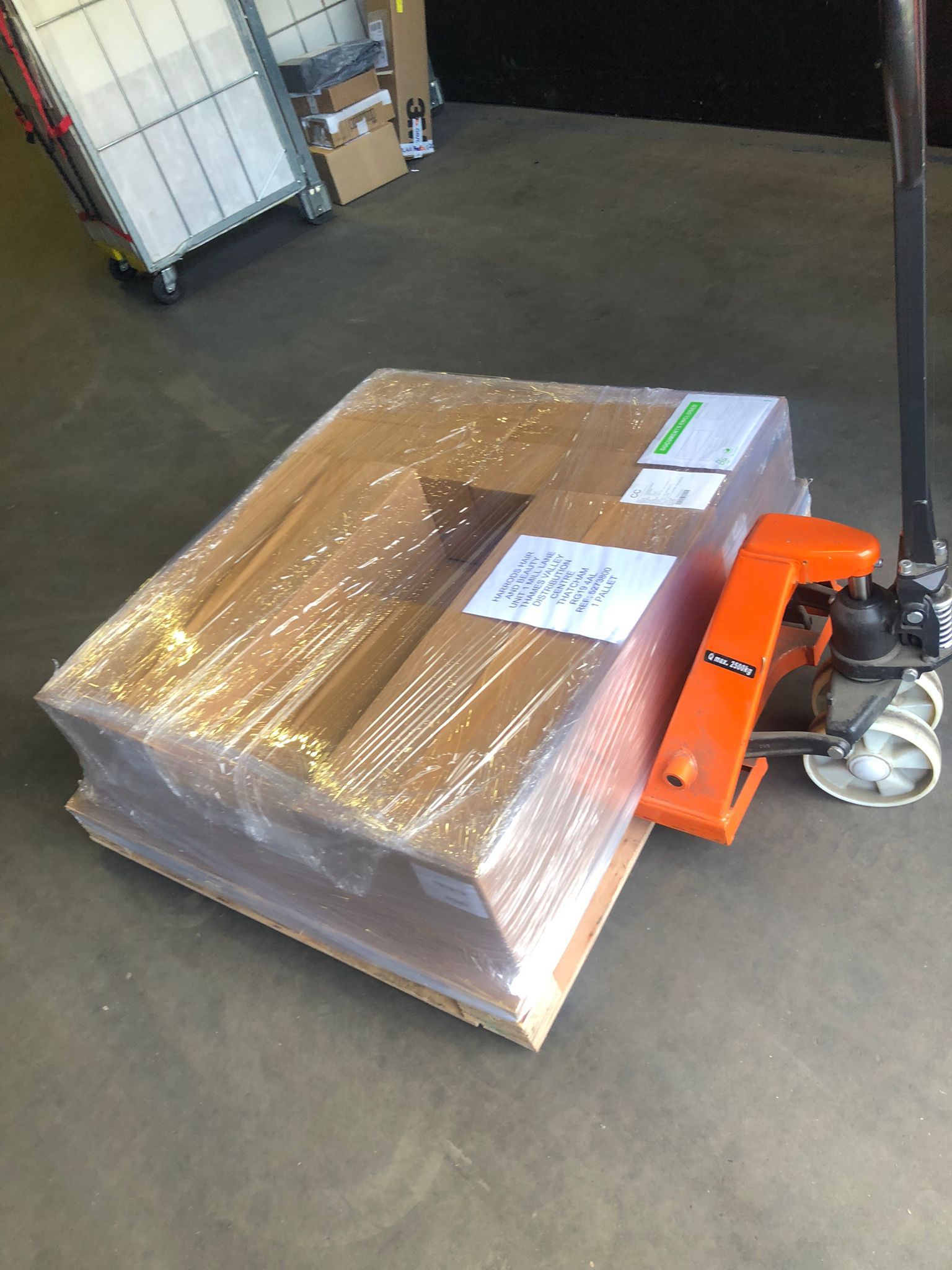 Shrink-wrapped pallet with boxes and an orange hand pallet jack on a warehouse floor