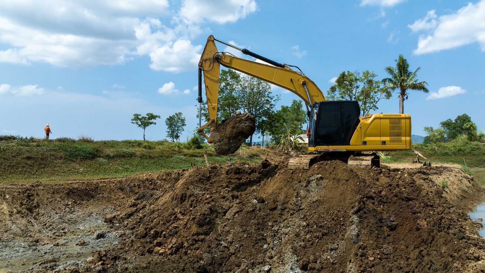 Yellow excavator digging in a muddy field under a blue sky.