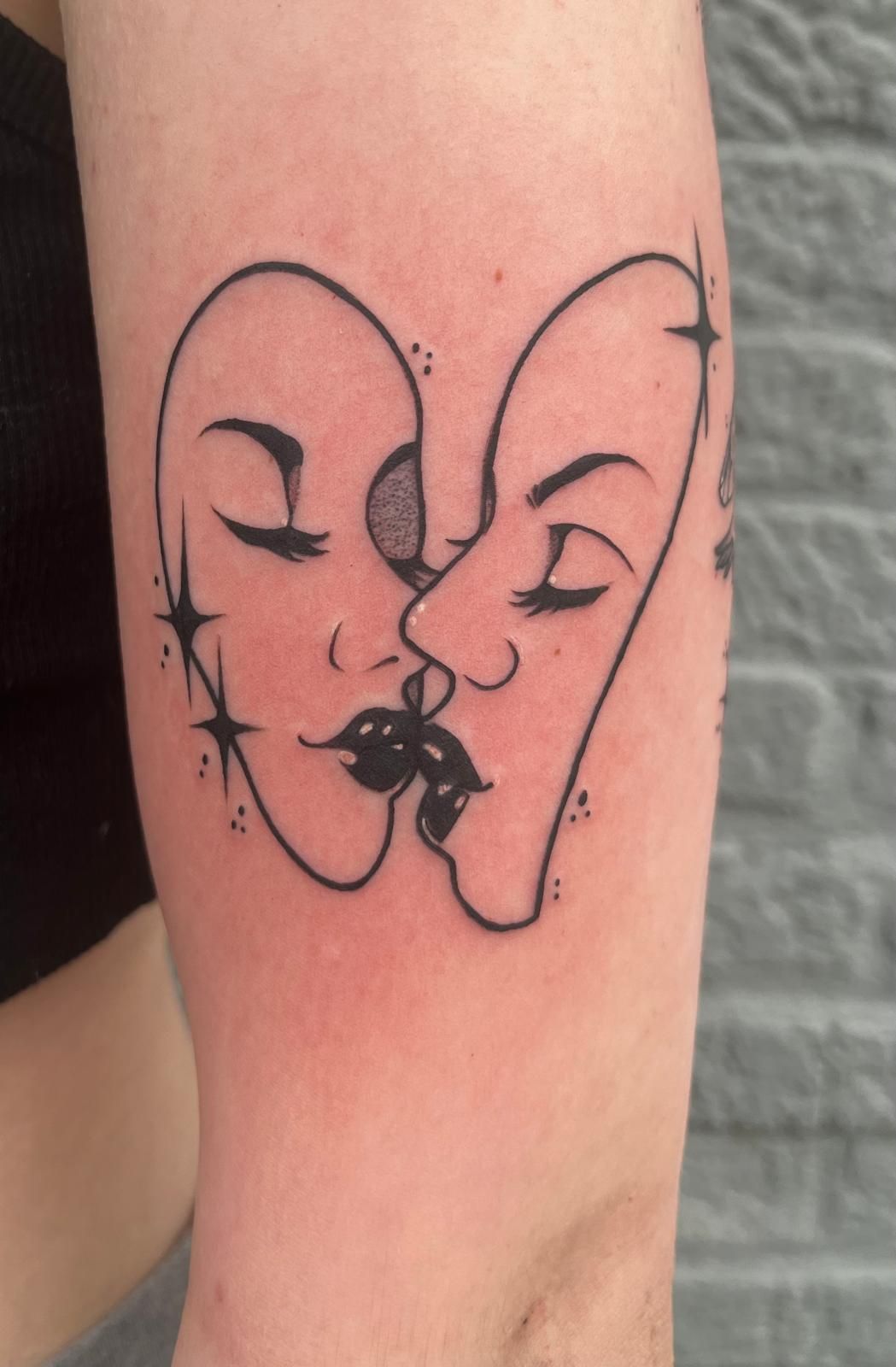 A tattoo of two faces kissing on a person 's arm