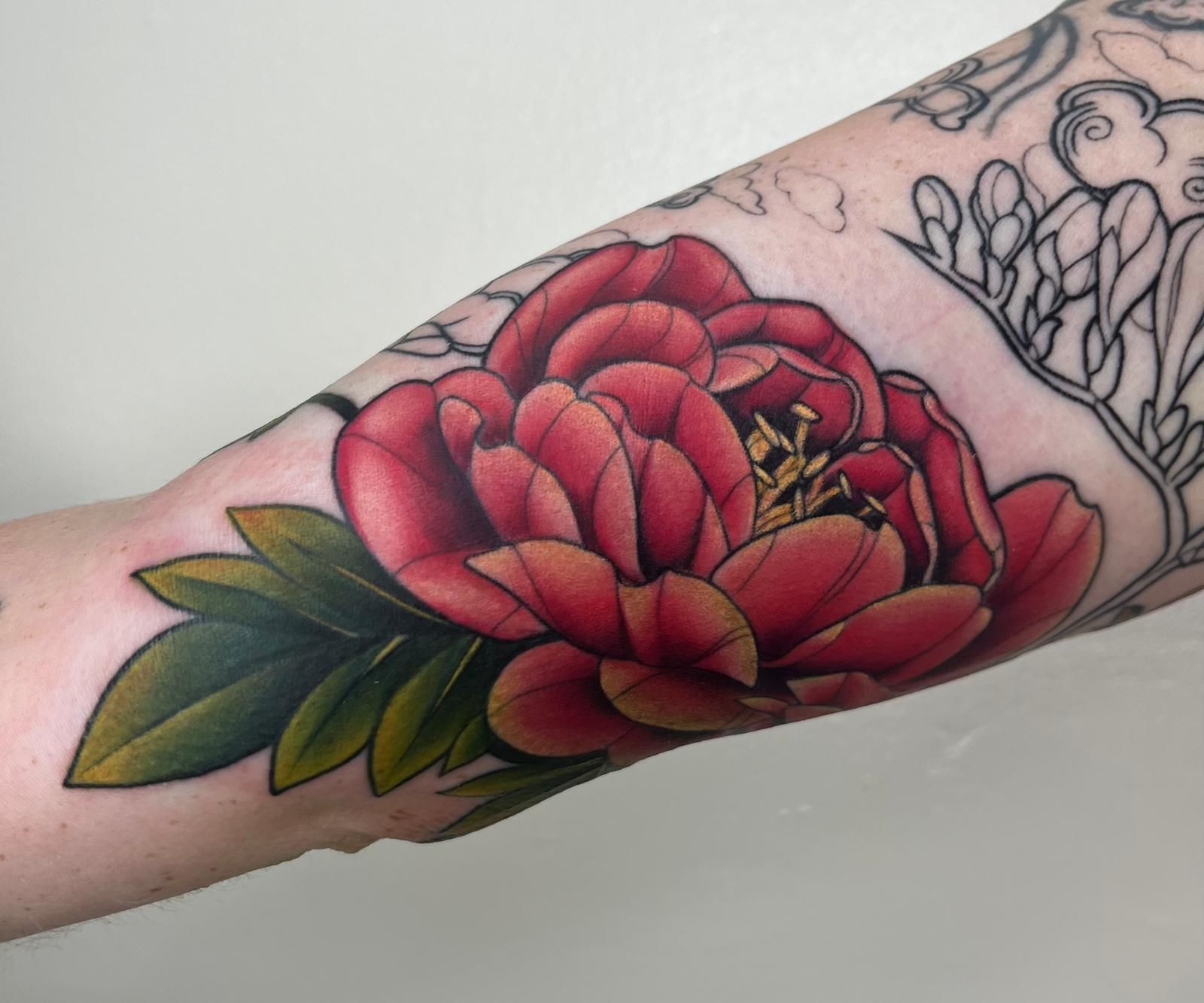 A woman has a tattoo of a red flower on her forearm
