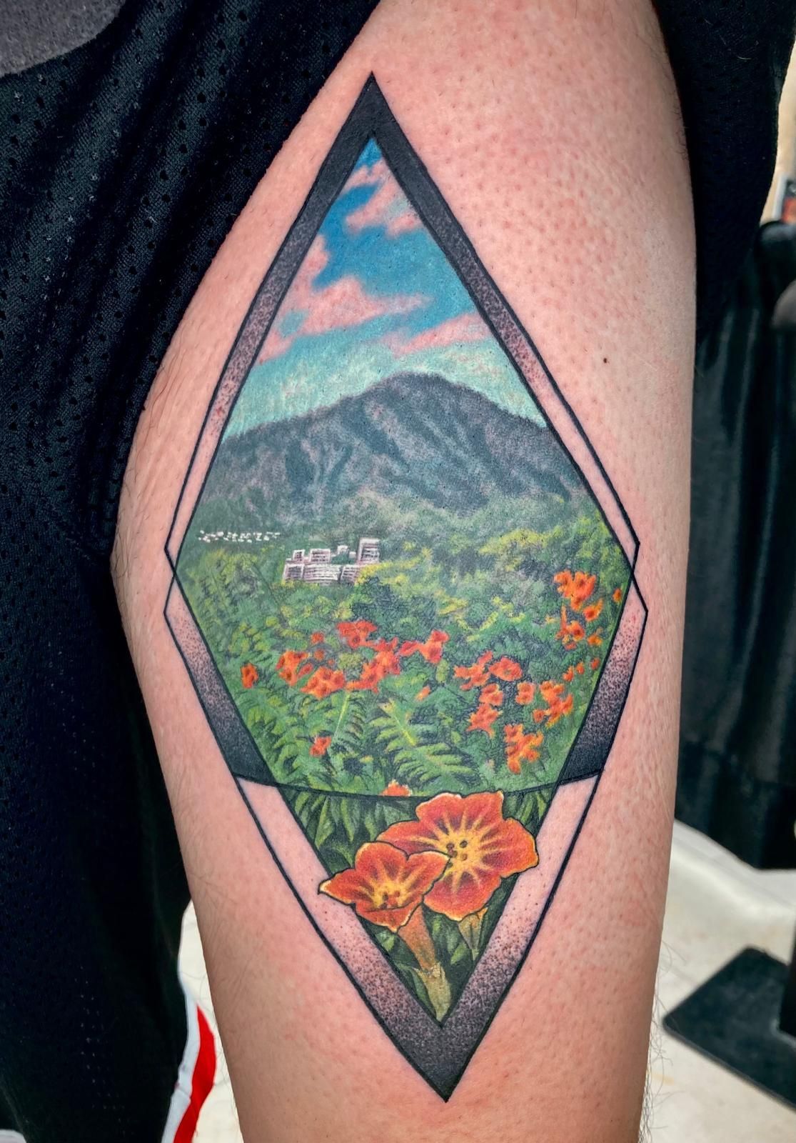 A person has a tattoo of a mountain and flowers on their thigh.