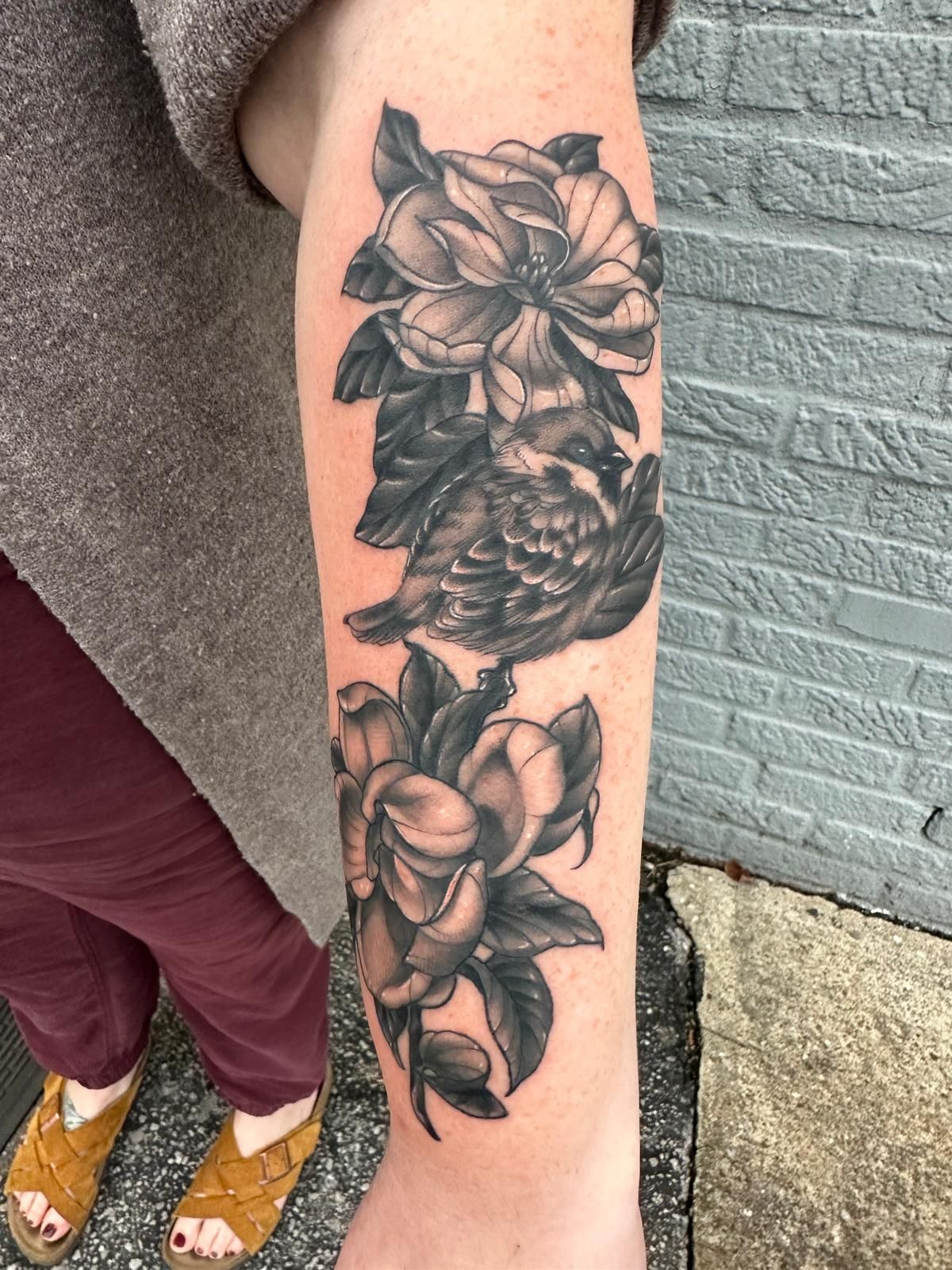 A woman has a tattoo of flowers and a bird on her forearm.