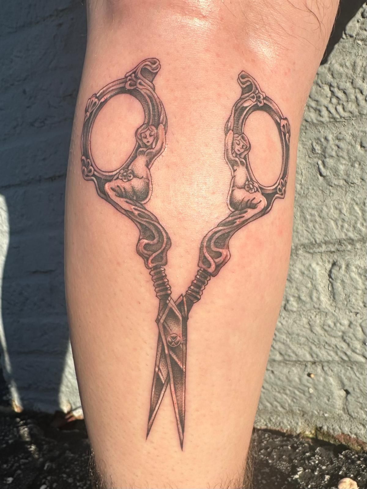 A person has a tattoo of a pair of scissors on their leg