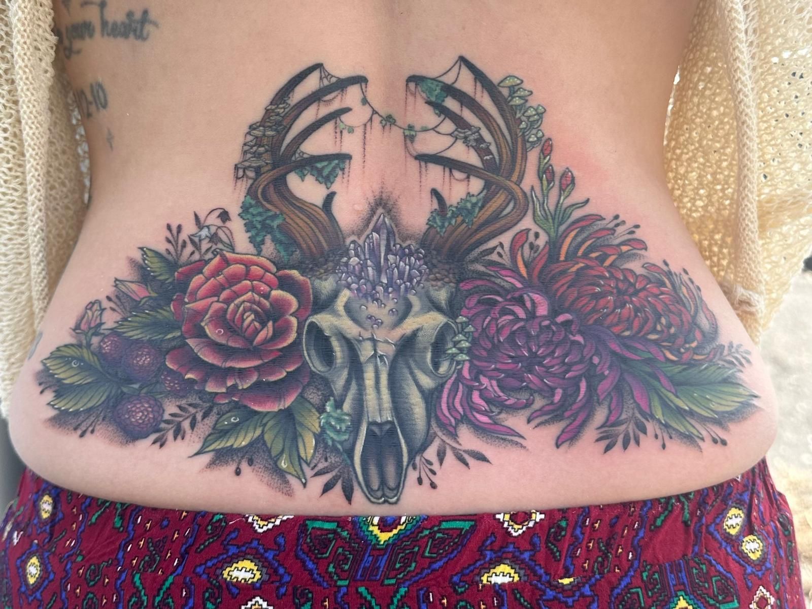 A woman has a tattoo of a deer skull and flowers on her back