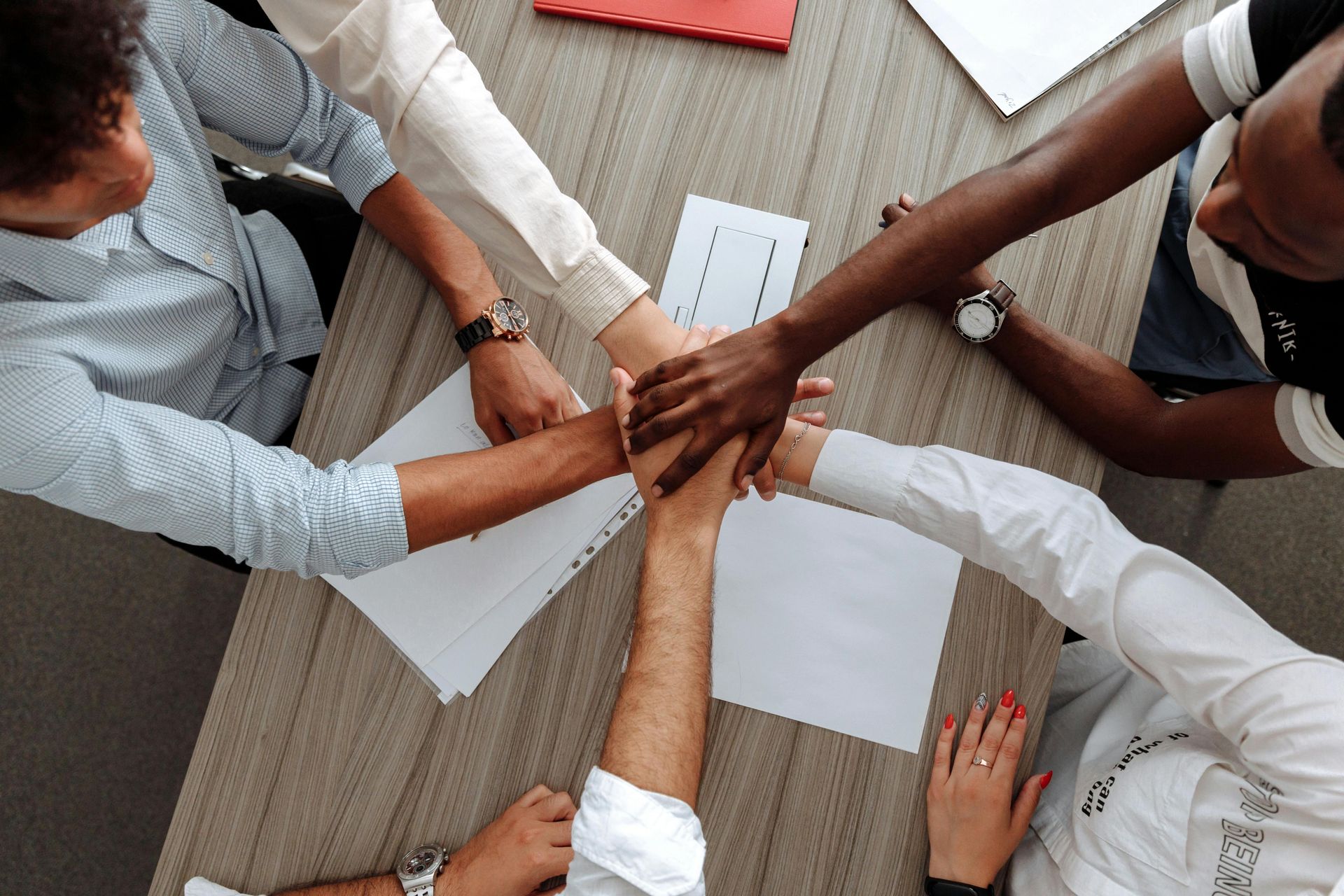 Hands of diverse people in a team huddle over a table with papers, symbol of collaboration.