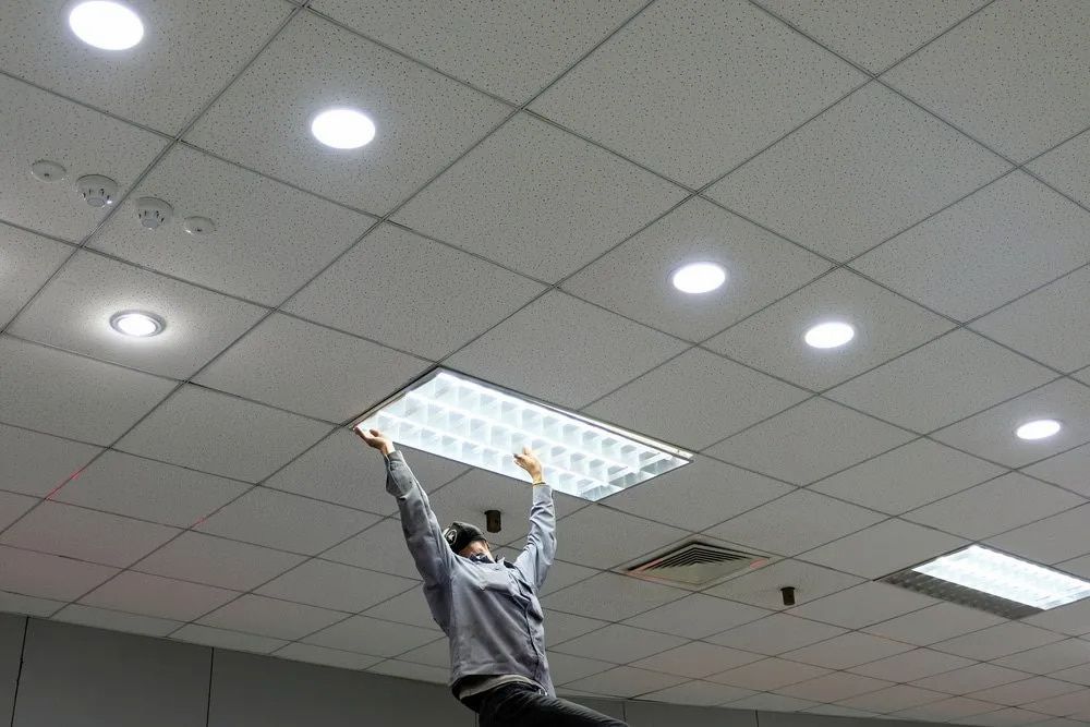 A Man is Hanging a Light Fixture From the Ceiling — Russell Taber Electrical & Solar in Lake Albert, NSW
