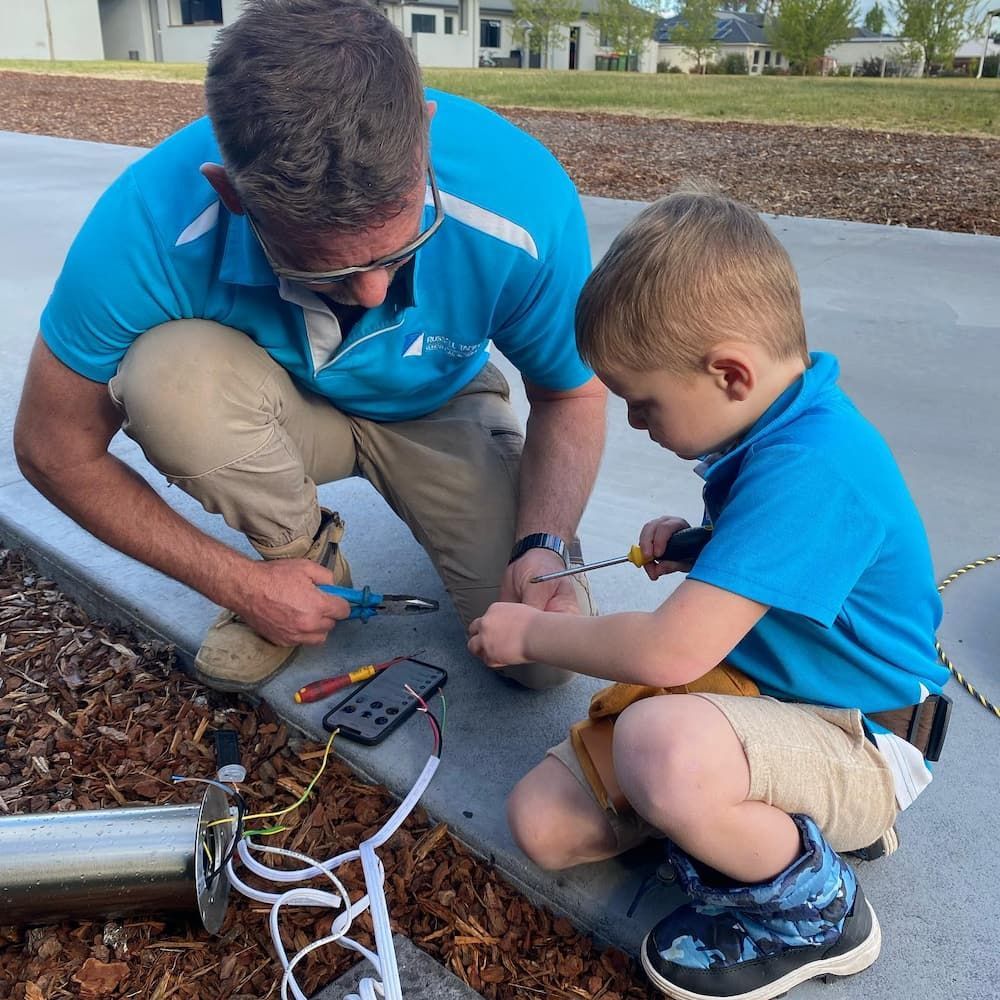 A Man and a Little Boy Are Working on a Device — Russell Taber Electrical & Solar in Lake Albert, NSW
