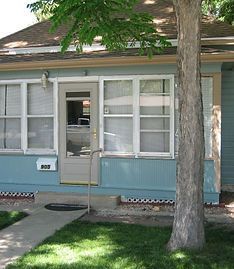 The front view of a blue house with white trim, a central door, multiple windows, and a tree in the front yard.