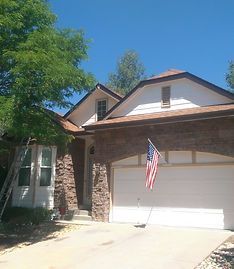 A one-story suburban house with a stone facade, a two-car garage, and an American flag hanging by the entrance.