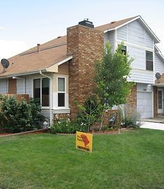 A two-story suburban house with brown roofing, light blue siding, and a brick chimney, seen from the front lawn.