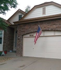 A tan suburban house with stone siding and an American flag mounted above the two-car garage.