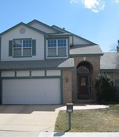 A two-story suburban house with a tan brick and beige siding facade, a front garage, and an arched entryway.