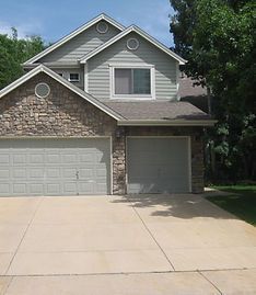 A two-story house with a beige siding upper level, a stone-accented front, and a three-car garage with a concrete driveway.