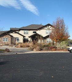 Large two-story house with stone and beige siding, a dark roof, and a paved circular driveway on a sunny day.