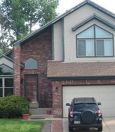 A two-story suburban home with brick and beige siding, a garage, and a dark SUV parked in the driveway.