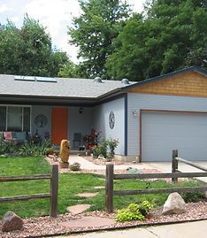 A gray single-story house with an orange front door, a two-car garage, and a wooden split-rail fence in the front yard.