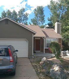 A single-story gray house with a garage, a brick-accented front entryway, and a driveway with a parked car.
