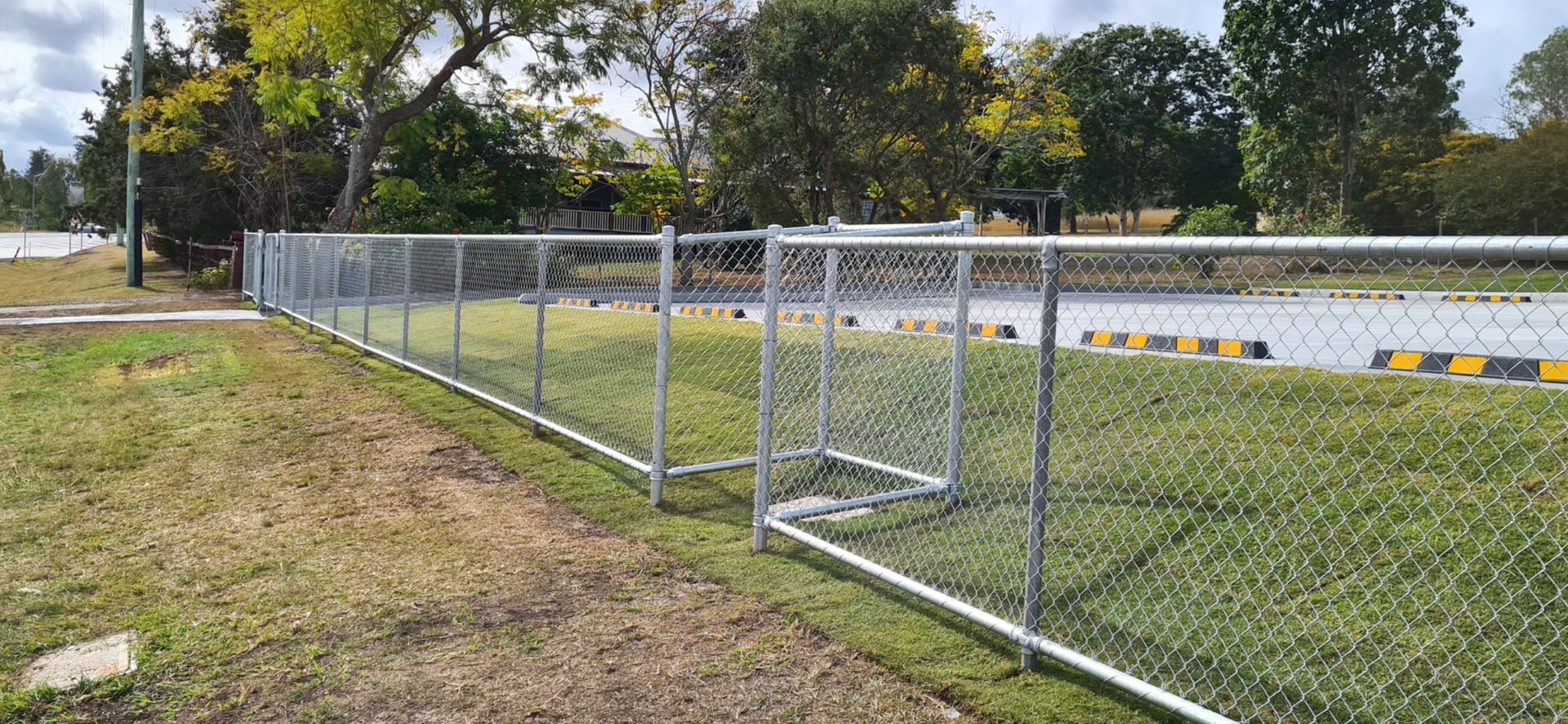 A Chain-link Fence Bordering a Grassy Area and an Asphalt — PROFENCE AND RETAINING in Beecher, QLD