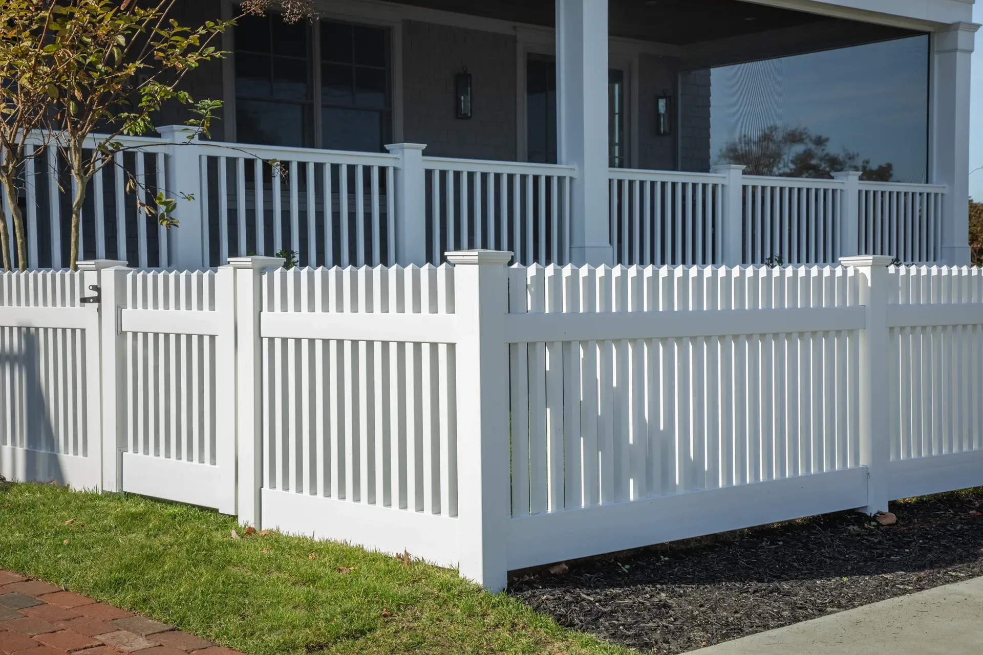 White picket fence surrounds a house with a porch.