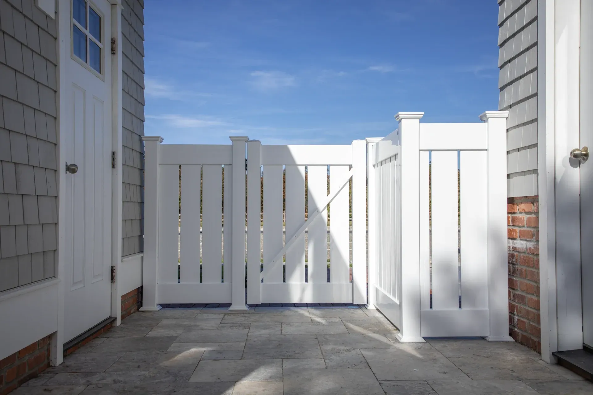 White wooden gate between buildings on a stone patio, with blue sky in the background.