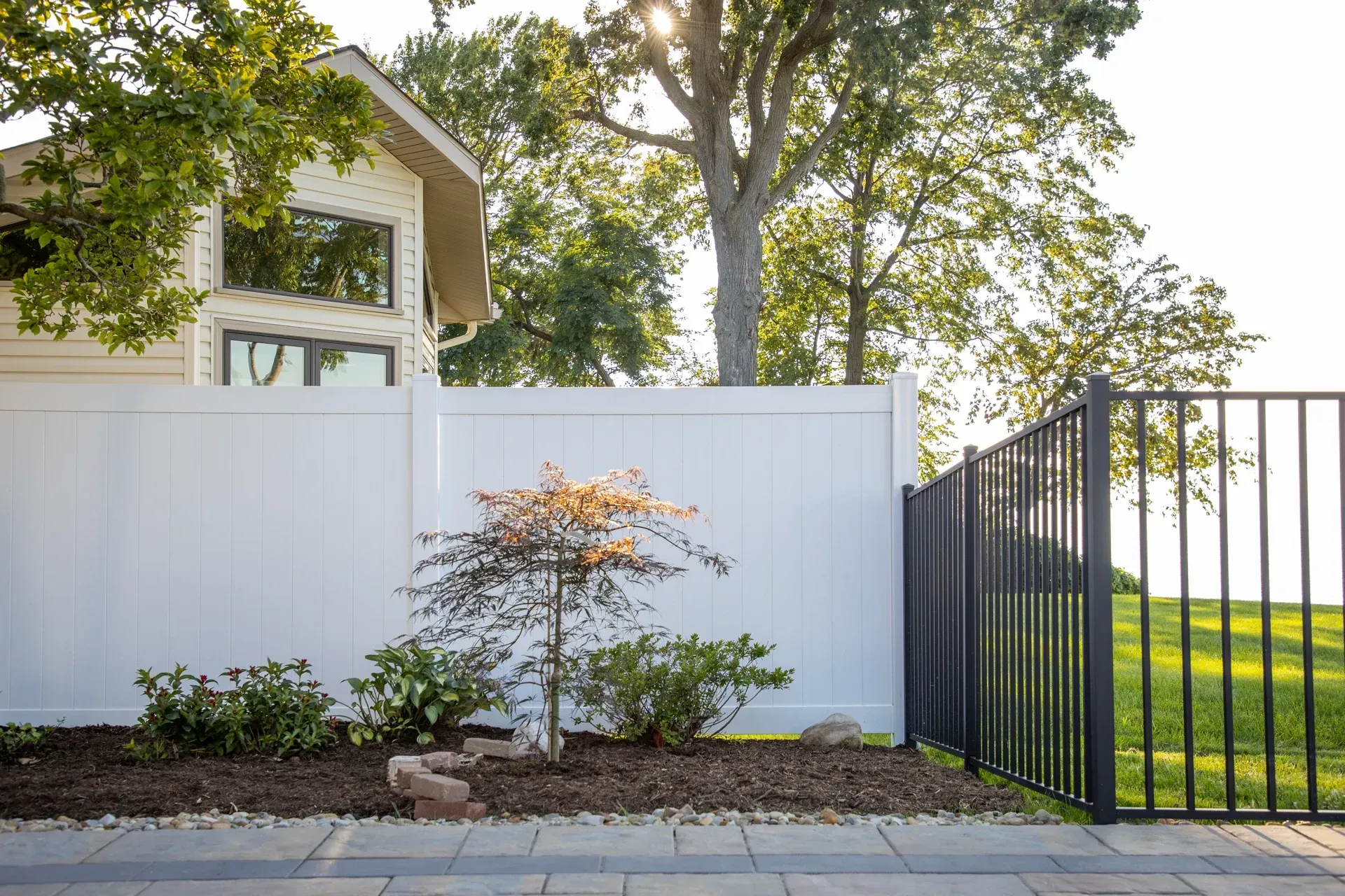 White privacy fence with black metal gate and small tree in front of a house.