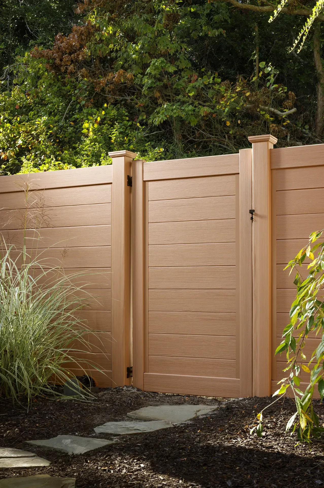Brown wooden gate and fence in a garden setting, with foliage in the background.