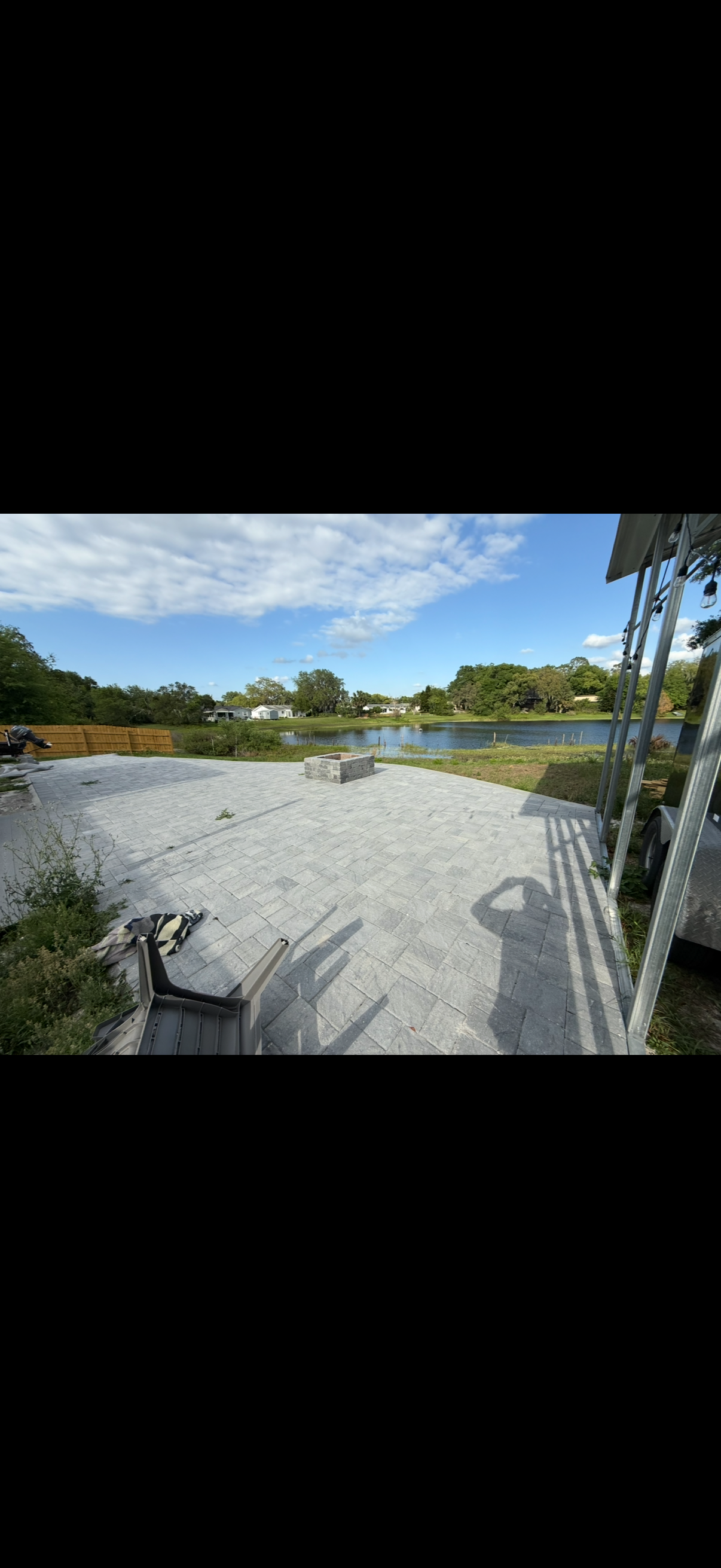 A gravel area next to a body of water with blue skies and trees in the background.