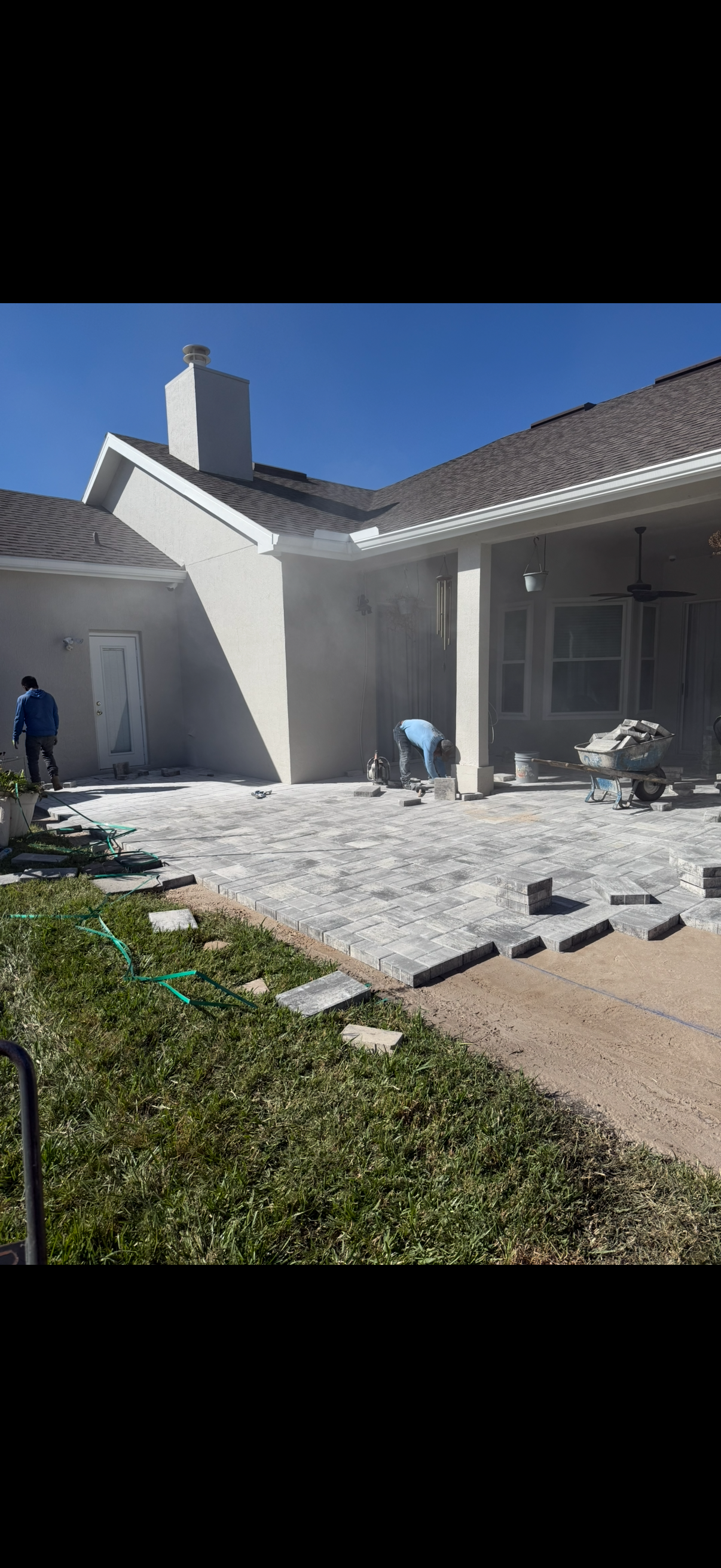 Workers installing a stone patio next to a house with a blue sky overhead.