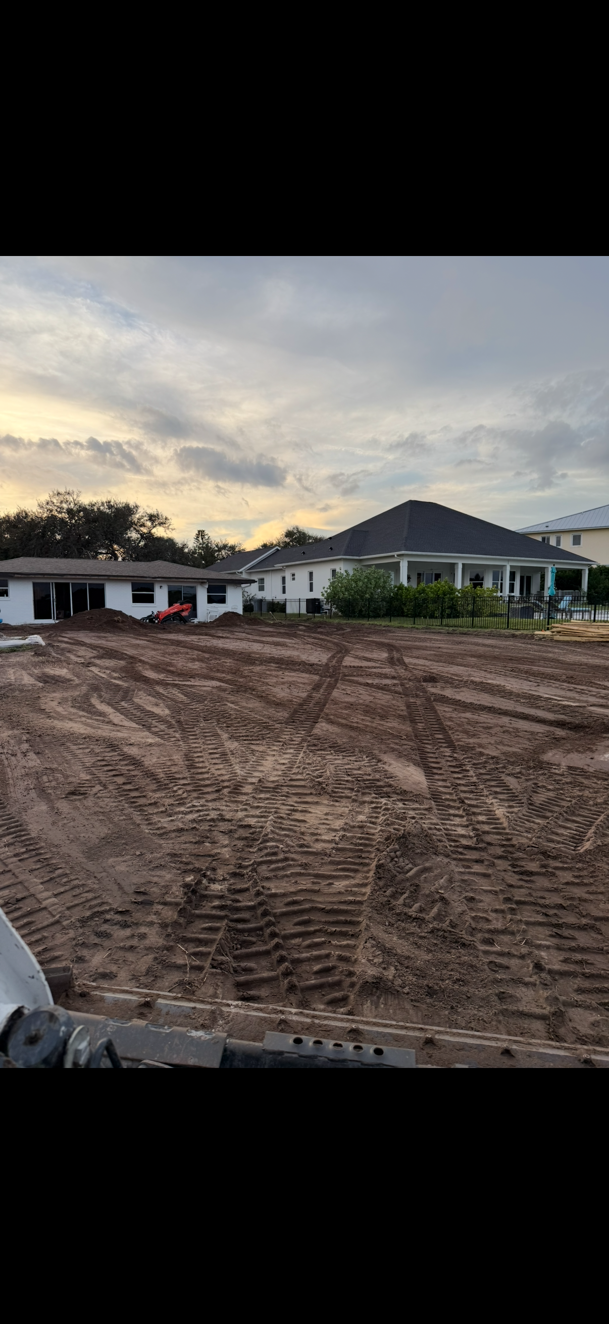 Cleared lot with a house under construction and another finished house under a cloudy sky.