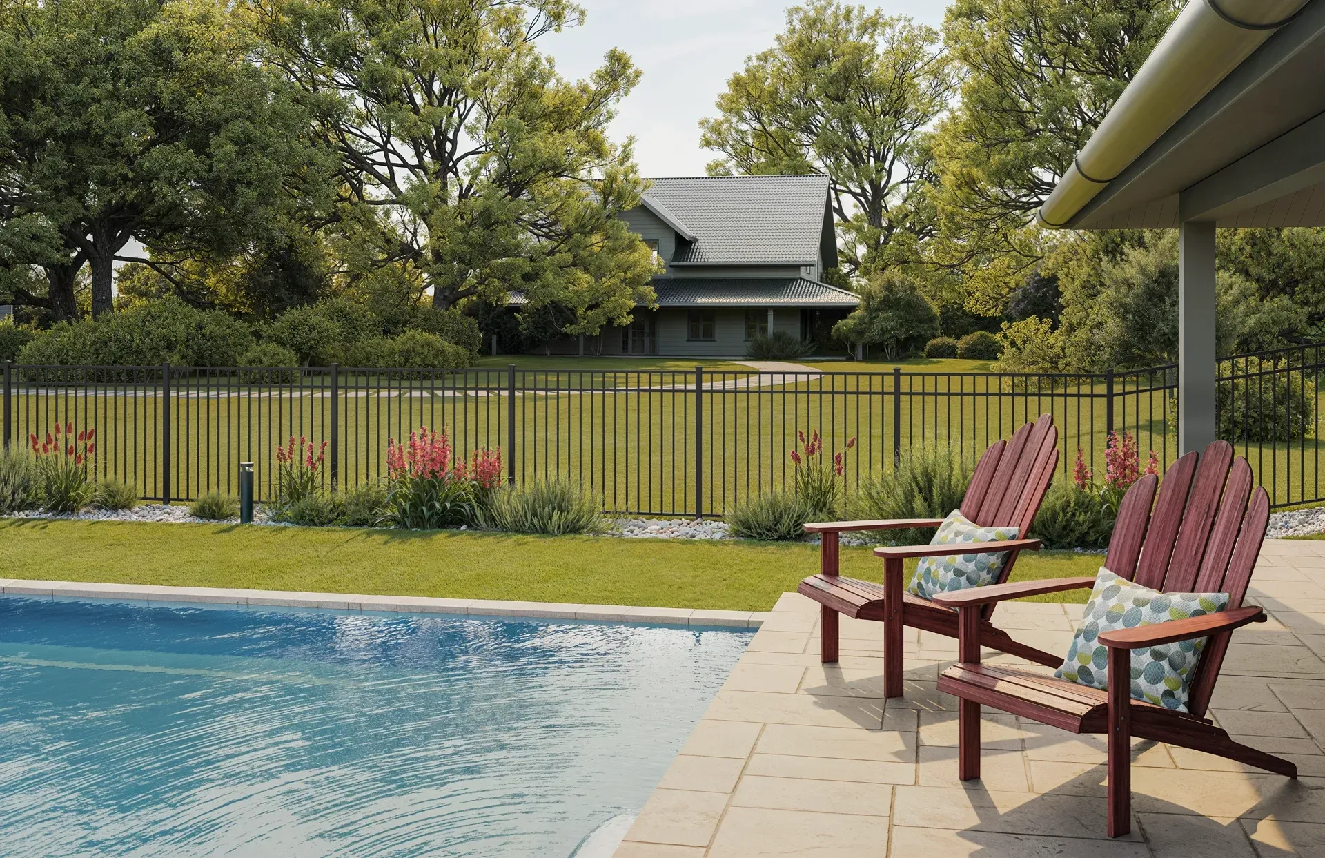 Two red Adirondack chairs on a patio beside a pool, overlooking a house and fenced yard with trees.