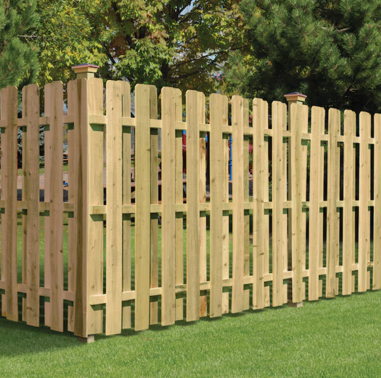 Wooden picket fence in a grassy yard, with trees in the background.