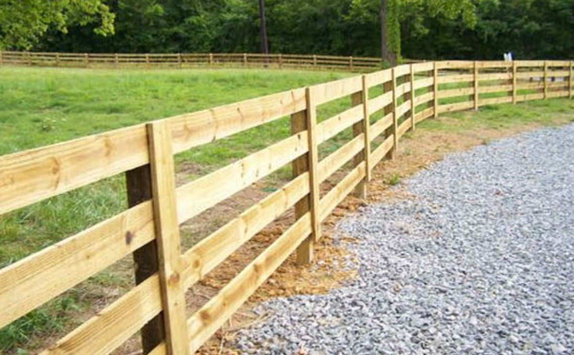 Wooden fence bordering a gravel driveway and green field.