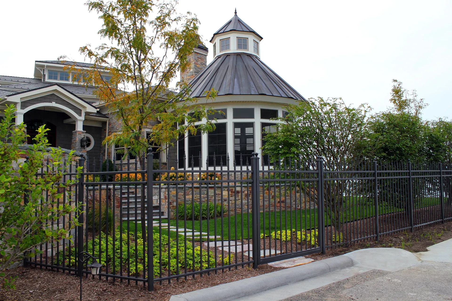 Black metal fence surrounding a building with a round, domed section and a gray roof; trees and landscaping.