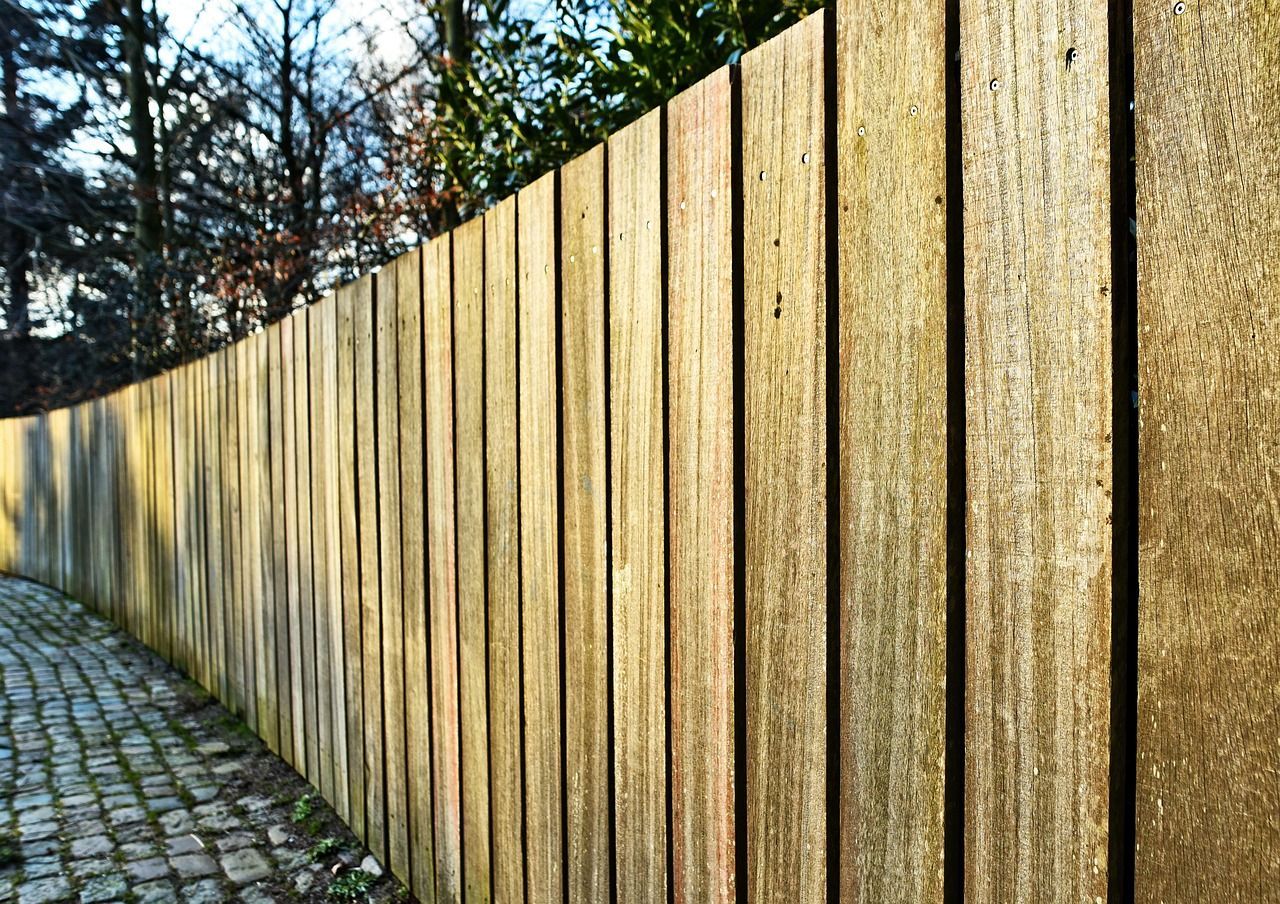 Wooden fence curving along a cobblestone path, with trees in the background.