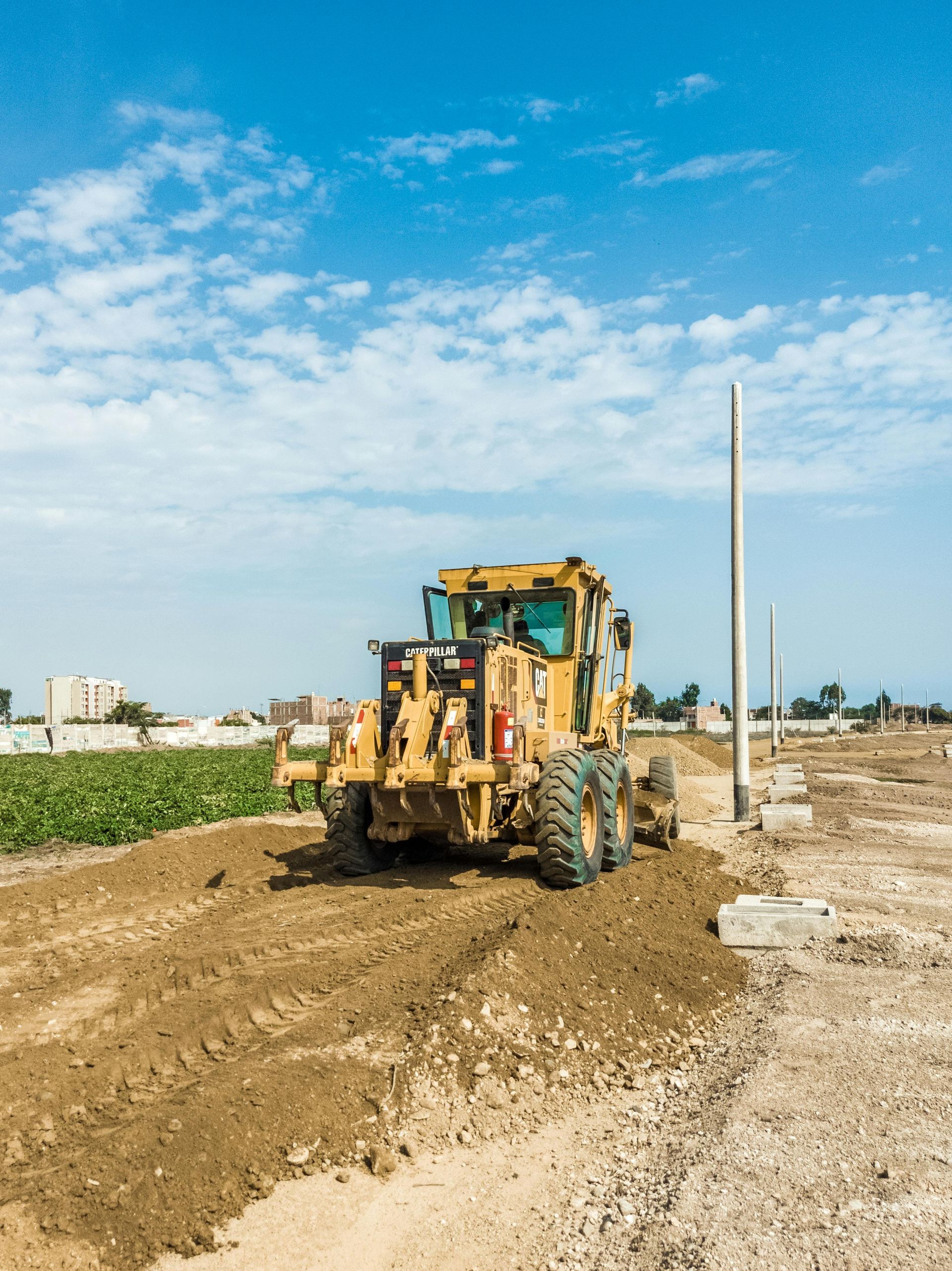 Yellow grader smoothing dirt on a construction site under a blue sky.