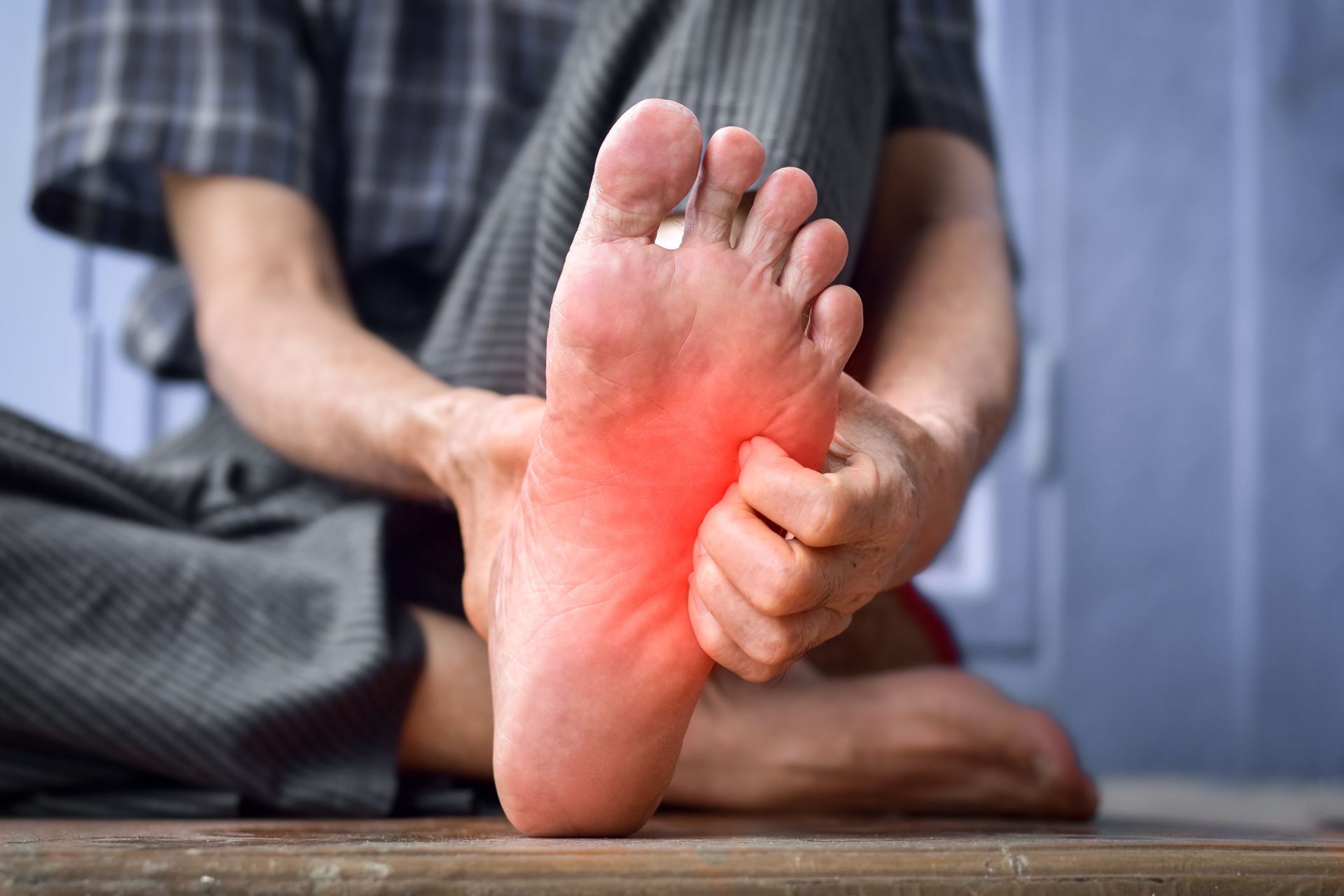 Person holding foot, highlighted area of redness, likely pain.