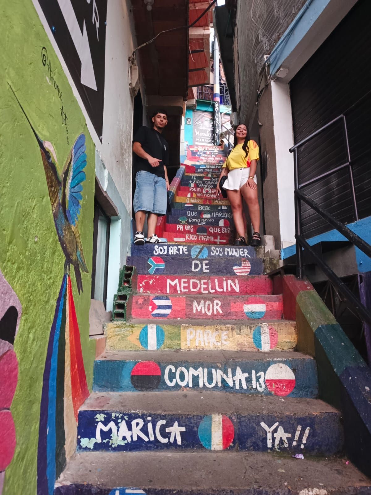 Dos personas se encuentran en unas escaleras pintadas de colores brillantes en la Comuna 13, Medellín, Colombia.