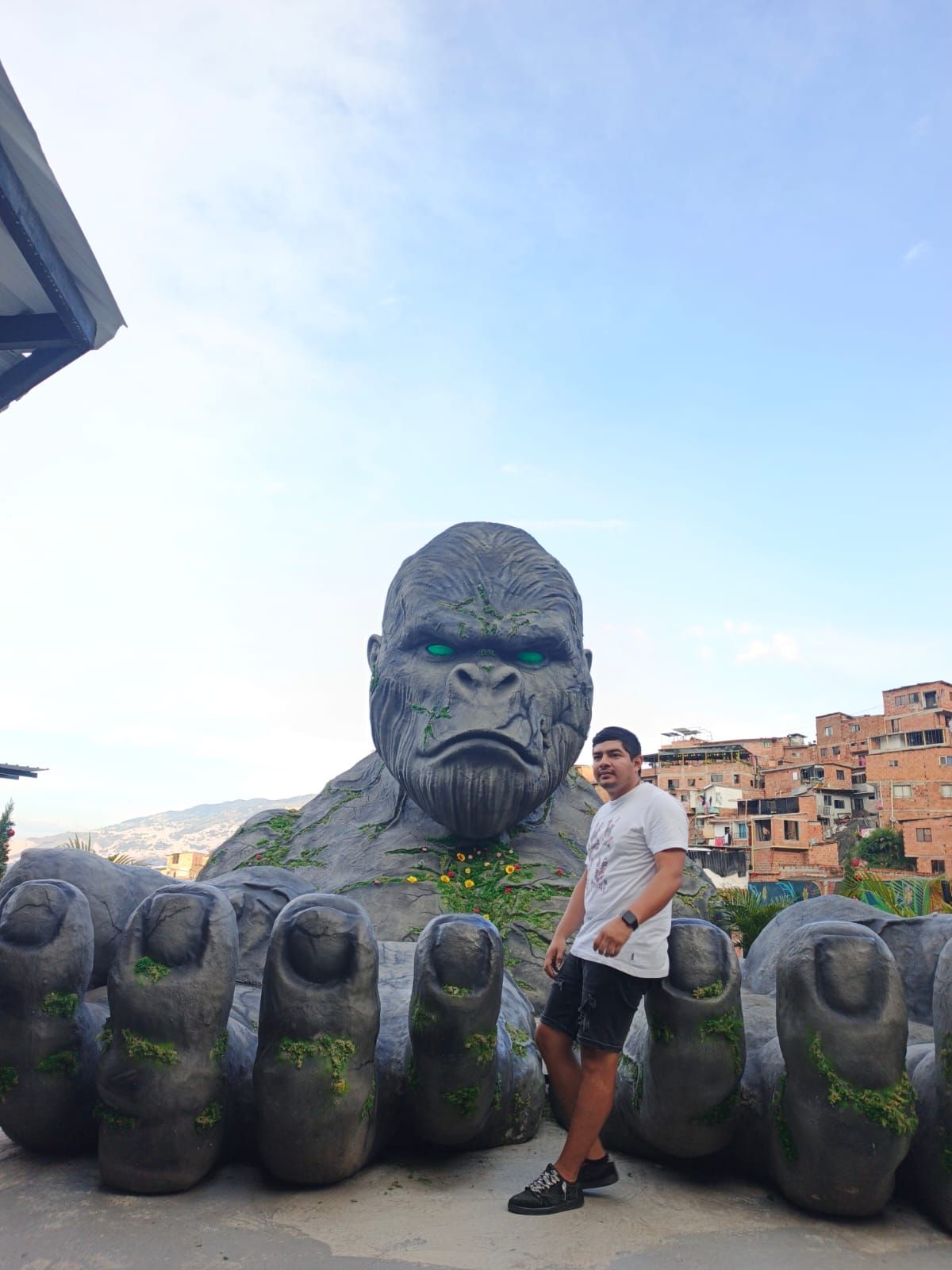 Un hombre posa cerca de una gran estatua de gorila en un entorno urbano.