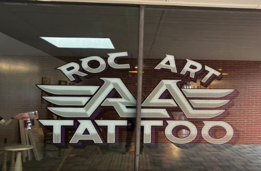 A man with a lot of tattoos is sitting at a table in a room.