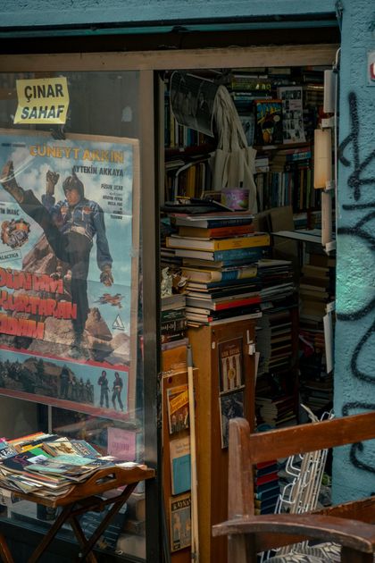 A bookstore entrance with a vintage movie poster in the window, stacks of books inside, and a wooden chair in the front.