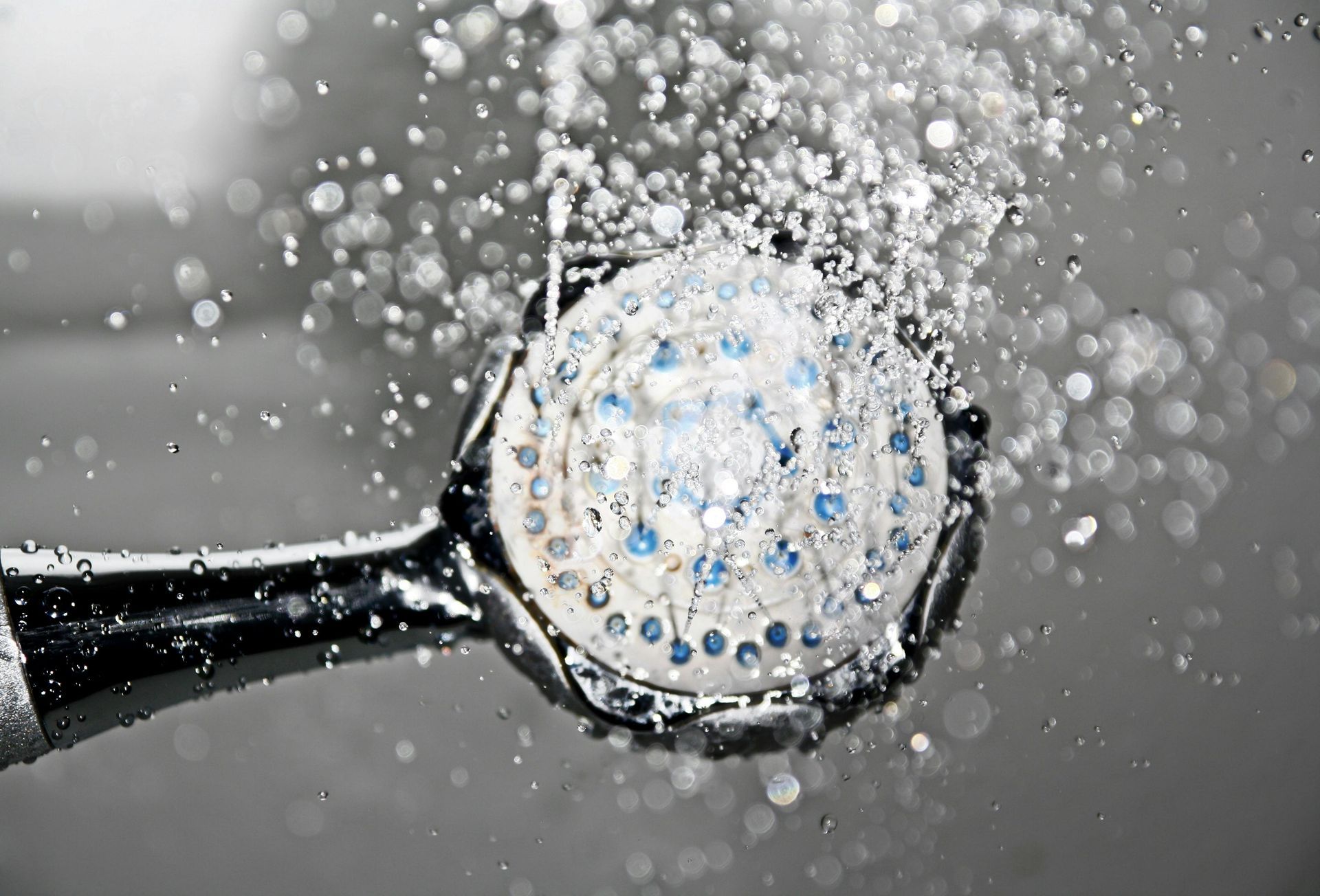 A chrome handheld showerhead spraying water droplets against a dark, neutral background.
